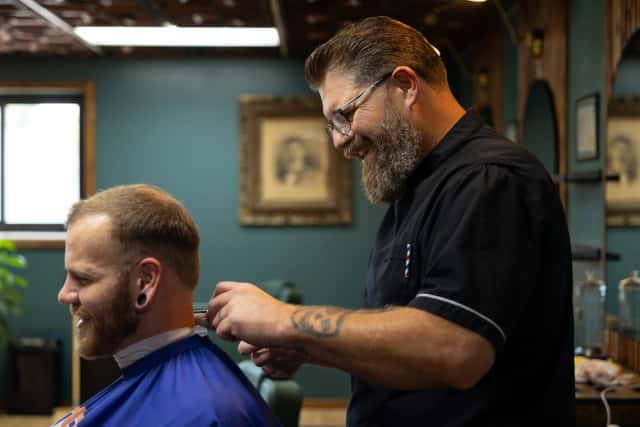 Professional barber Tim trimming client beard with straight razor at Cache Cuts Logan